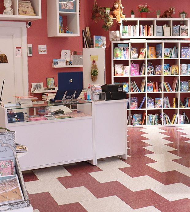 Vista del interior de la librería, dónde podemos ver el mostrador, delante de una puerta, estanterías con libros al fondo y atisbo de un expositor en primer plano