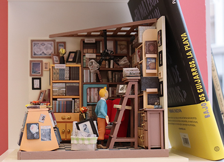 Primer plano de un sujeta libros que representa una habitación estanterías llenas de libros y a Tintin mirándo los libros