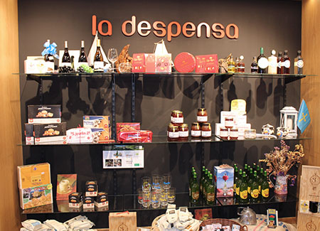 Vista del interior del comercio dónde vemos un expositor de baldas de cristal con diversos productos de origen asturiano bajo el cartel: la despensa