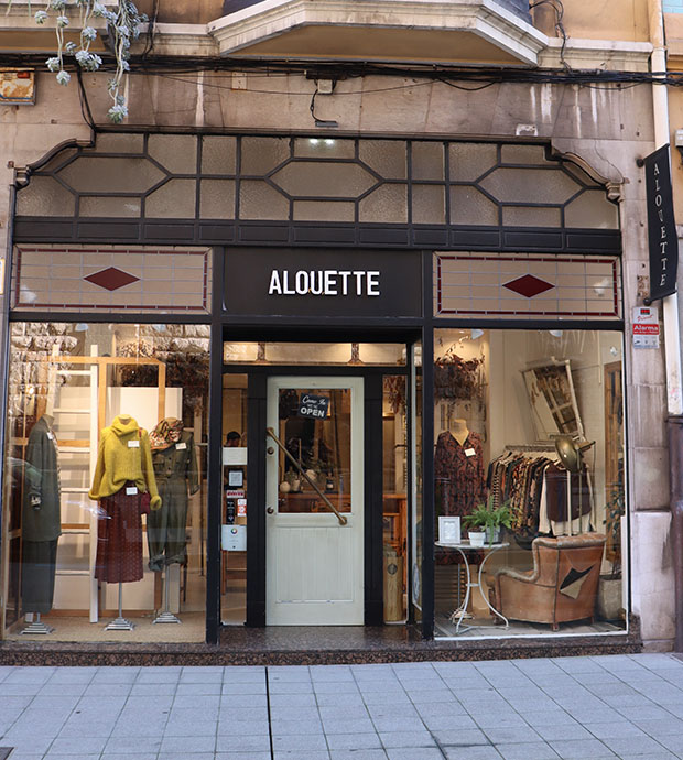 Vista del exterior de la tienda, dónde podemos ver la puerta de entrada así como los dos escaparates a ambos lados de la misma. La puerta está metida más hacia el interior que los escaparates