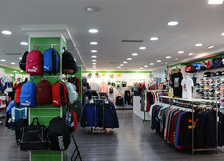 Vista del interior de la tienda, dónde podemos apreciar el tamaño de los pasillos. También vemos percheros y estanterías con ropa, mochilas y deportivas