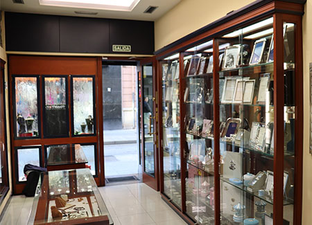 Vista desde el interior de la joyería de la entrada de la misma. También se ve una estantería cerrada y un expositor, ambos de madera y cristal