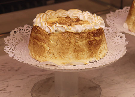 Primer plano de un postre adornado con merengue requemado, sobre un pedestal con puntilla