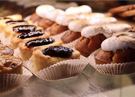 Primer plano de pasteles cubiertos por mermelada y por merengue requemado. Todos los pasteles descansan sobre papeles de magdalena