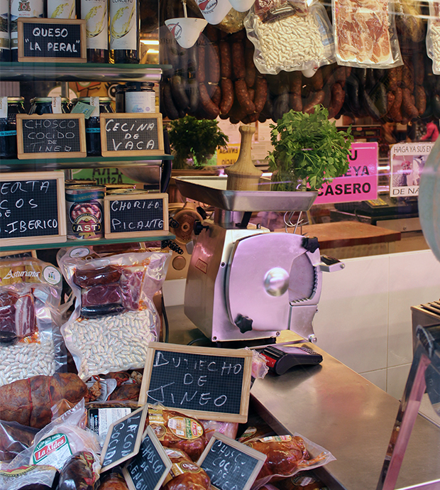 Vista del interior de la carnicería, dónde podemos ver un lateral del mostrador, en el que hay pizarras para anunciar productos, embutidos, paquetes al vacío para hacer fabada y una máquina de corte