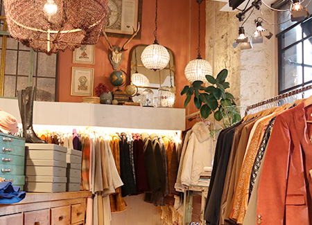 Vista del interior de la tienda, dónde se puede ver un perchero de pared al fondo, uno de pie en primer plano y un expositor con botas y otros complementos