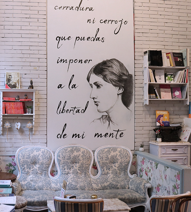 Vista del interior de la librería, dónde podemos ver un mural, unas estanterías con libros y un sofá junto a una mesa con sillas