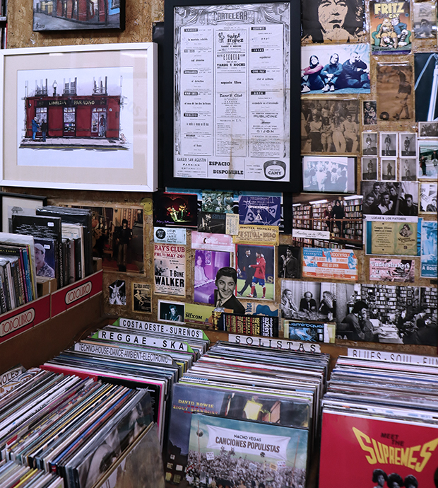 Primer plano de un expositor de discos de vinilo, en la pared de detrás podemos ver fotos, postales y carteles antiguos. En el lado izquierdo se ve parcialmente un expositor de libros