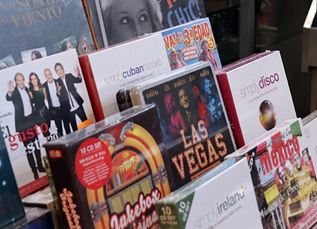 Primer plano de un expositor con varios sets de CD de música de diversos estilos. Al fondo se ven las portadas de dos discos de vinilo.